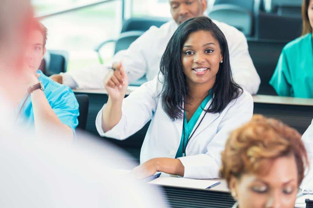 Young adult African American doctor or nurse sitting in meeting room at hospital, with diverse adminstrators, nurses, and students.