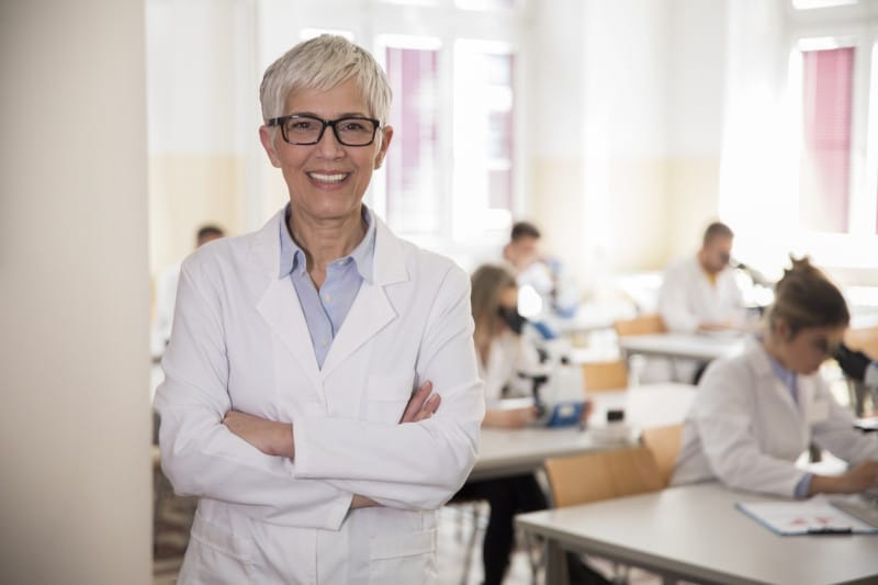 Medical science professor standing in front of a lab with student using microscopes professor standing in front of a students in laboratory