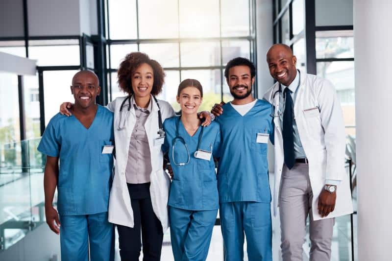 cheerful group of doctors standing with their arms around each other inside of a hospital during the day