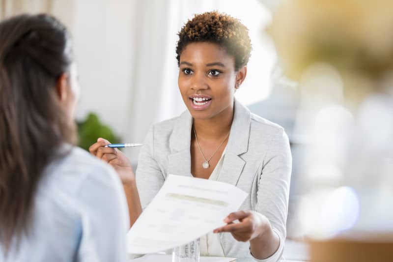 young woman in medical field has a serious expression on her face while discussing a document with a female colleague