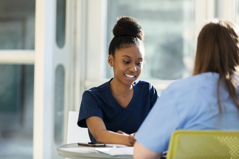 Med student talking to advisor about how GPA impacts med school applications two young adult female university students work together on a project for their medical science class