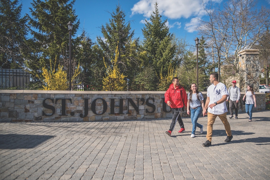 five college students walking in front of st johns university wall on campus