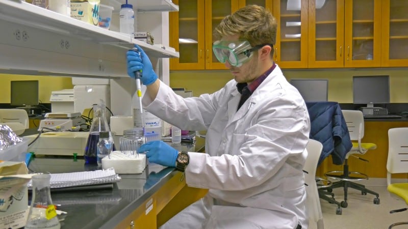 male pre-med student adding chemical to test tube in biochemistry lab class