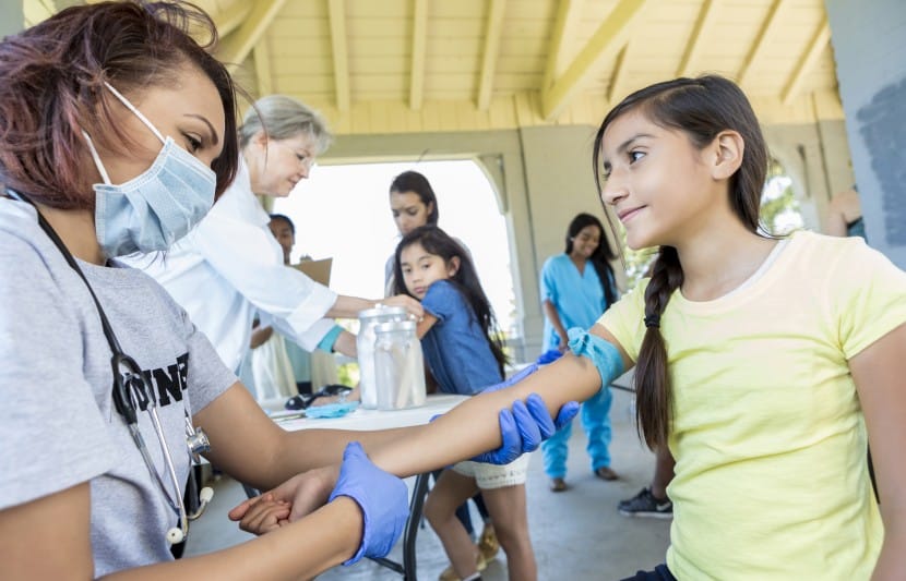 gap year pre-med student at community clinic checking preparing to imumize young hispanic girl