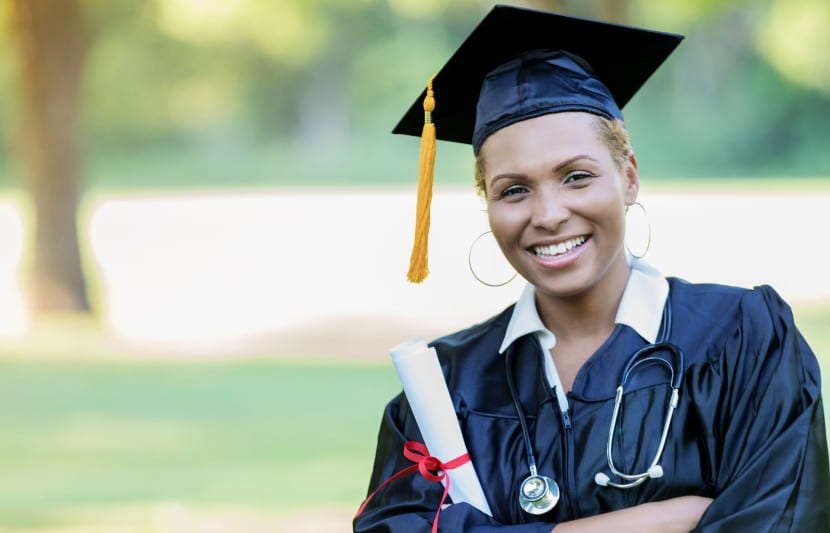female pre-med masters graduate wearing graduation gown, hat, and stethoscope around neck